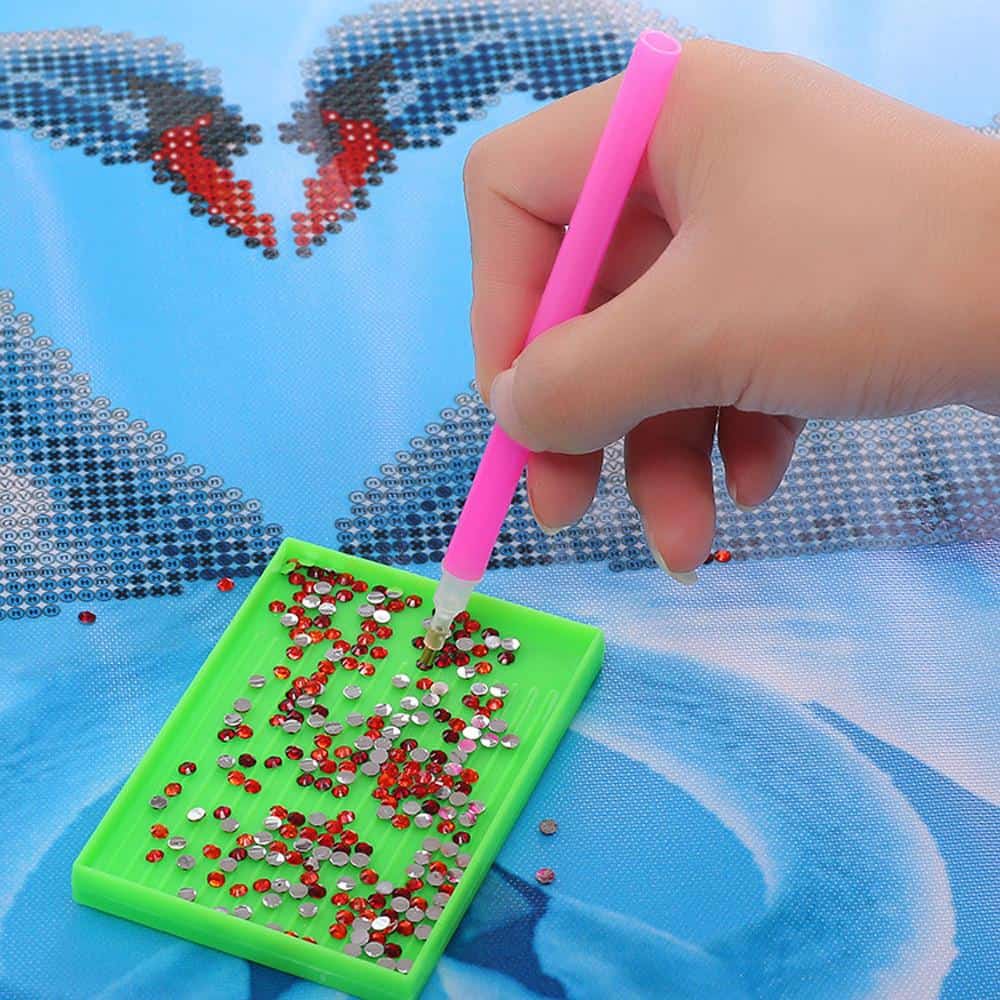 Hand placing red diamond drills onto a blue canvas with a pink applicator pen