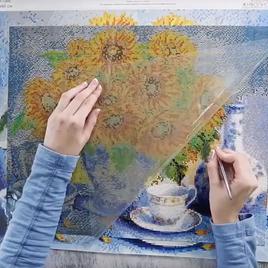 Hands applying drills to a diamond painting canvas with a pen and tray